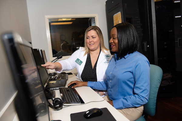 A nursing administrator working with a Health Informaticist at a computer.