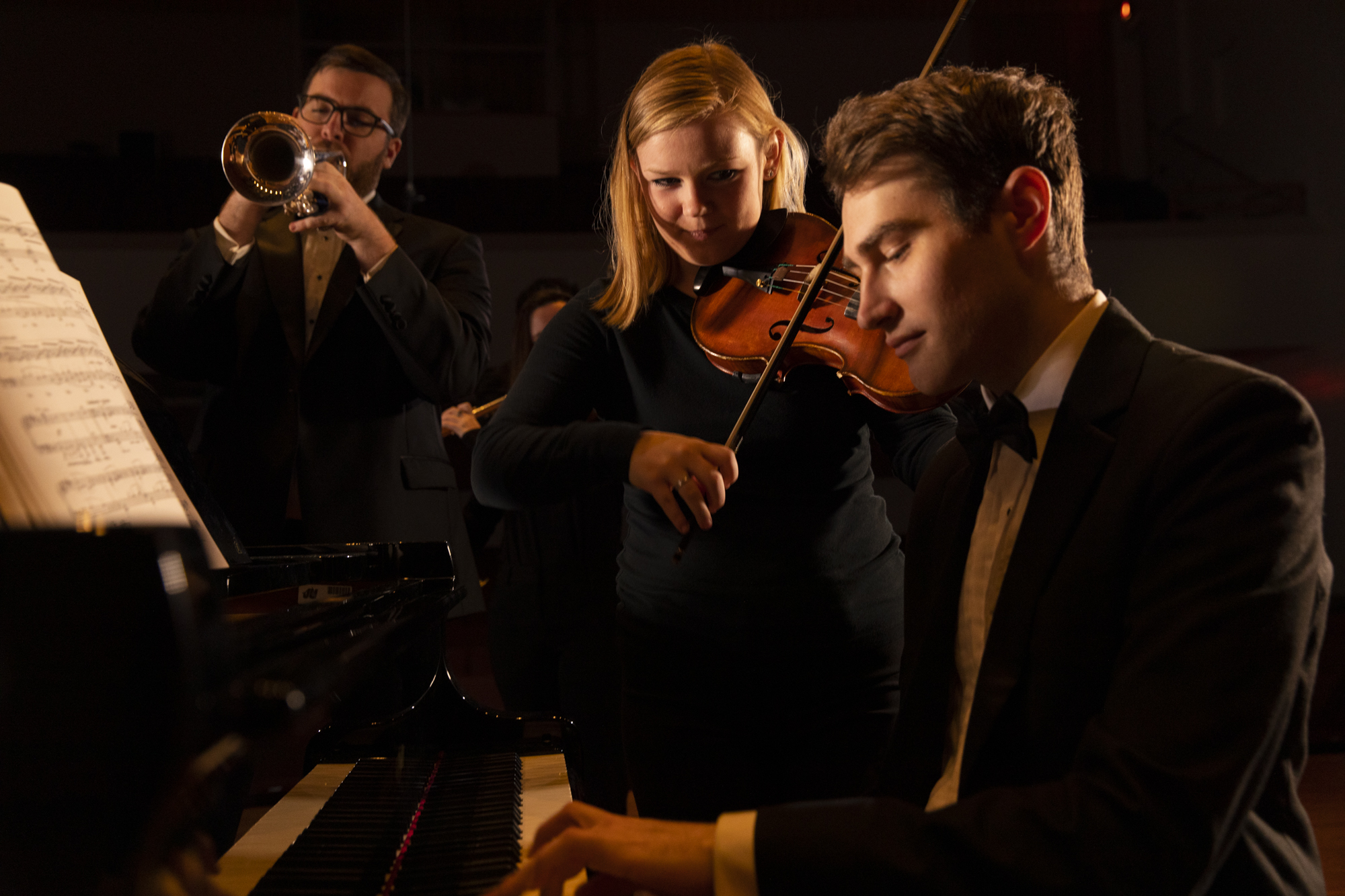 Three music students practicing piano, violin, and trumpet.